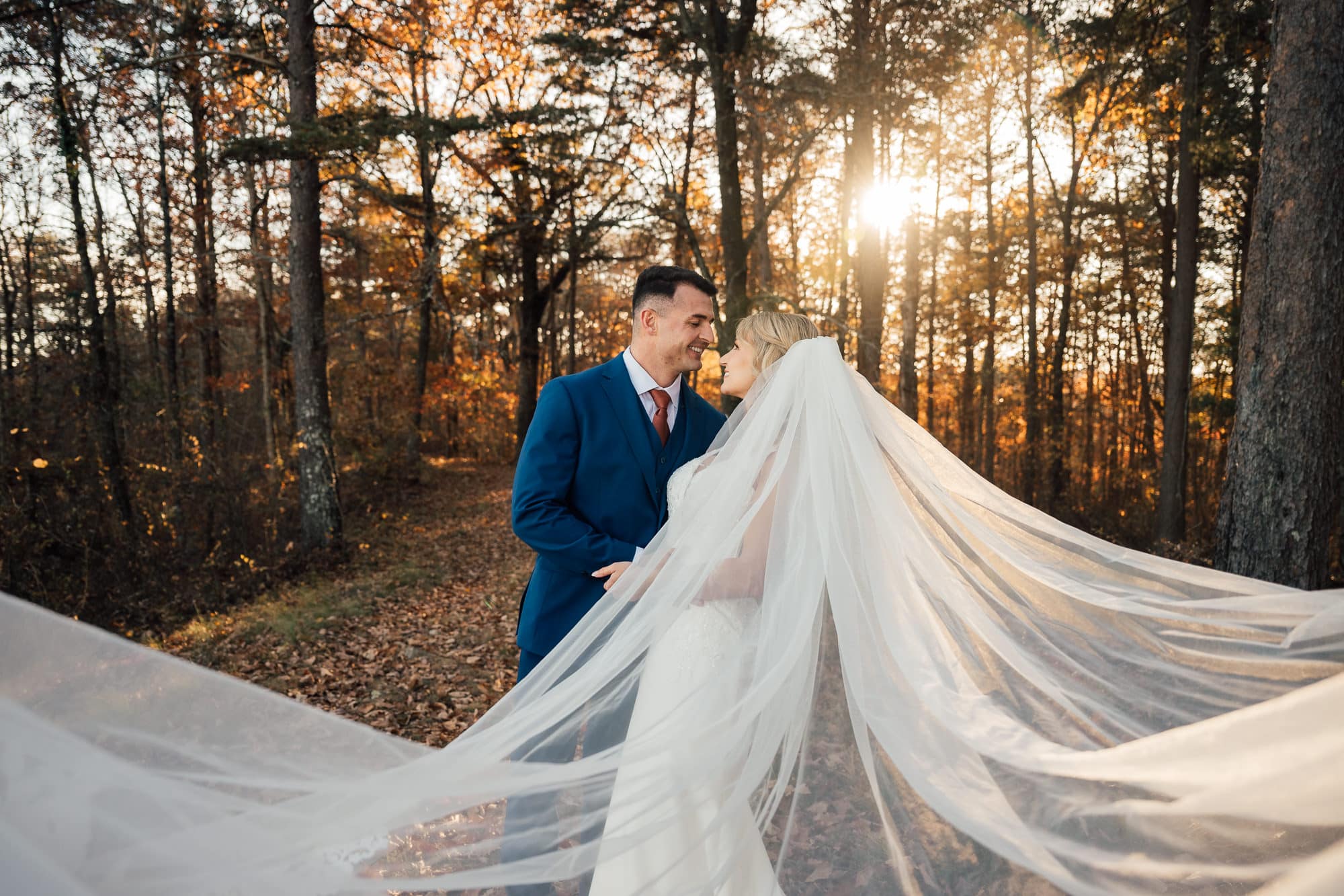 Couple embraces with veil glowing in sunlight. 